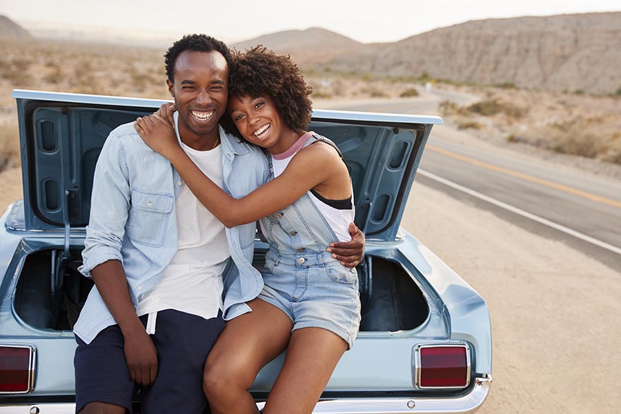 Personal Insurance - Couple With Their Arms Around One Another Sitting in the Back of Their Classic Car, Parked on a Desert Highway